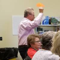 A man holding an orange piece of felt is walking to the front of the room